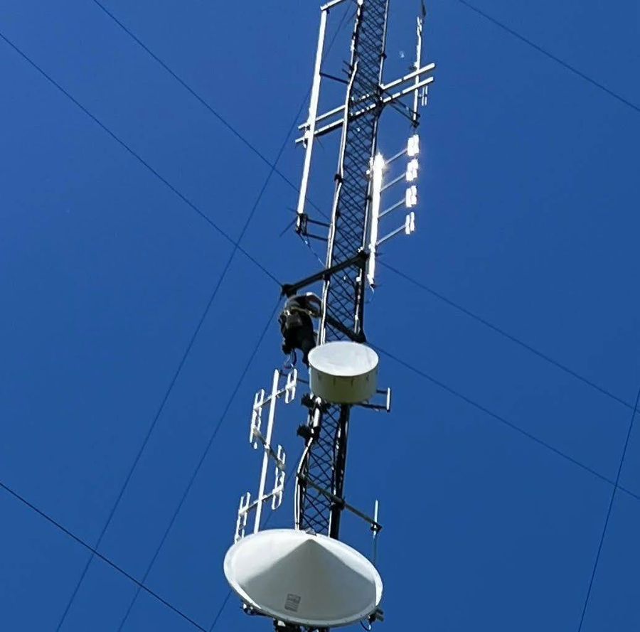 Technician climbing a lattice tower with antennas and microwave dishes